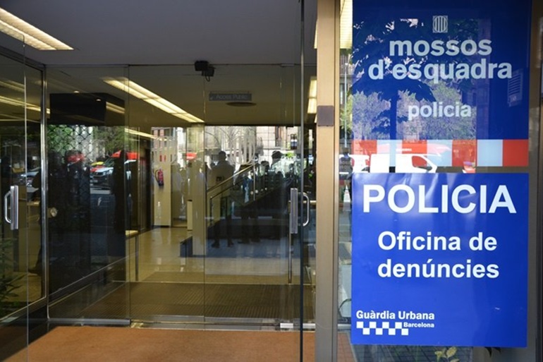 Acceso a una oficina de denuncias en Barcelona con señalización de Mossos d’Esquadra y Guardia Urbana.