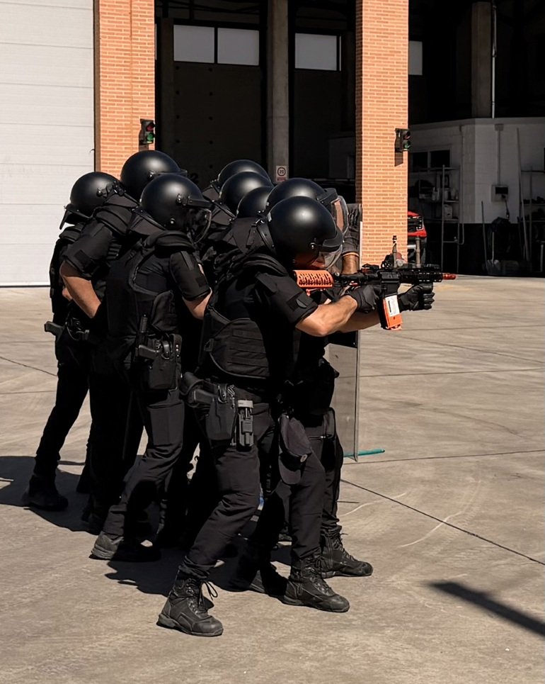 Grupo de agentes policiales con equipamiento táctico y escudos de protección durante un ejercicio de formación en técnicas de intervención y uso de dispositivos de lanzamiento.